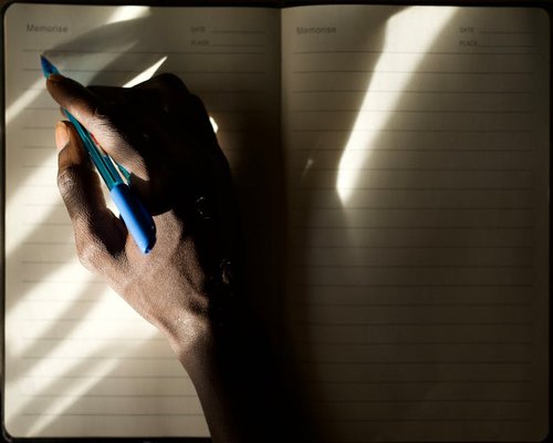 A person writing in a journal by a window with natural morning light
